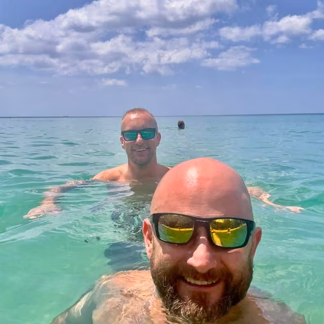 Two men in sunglasses swimming in clear turquoise ocean water